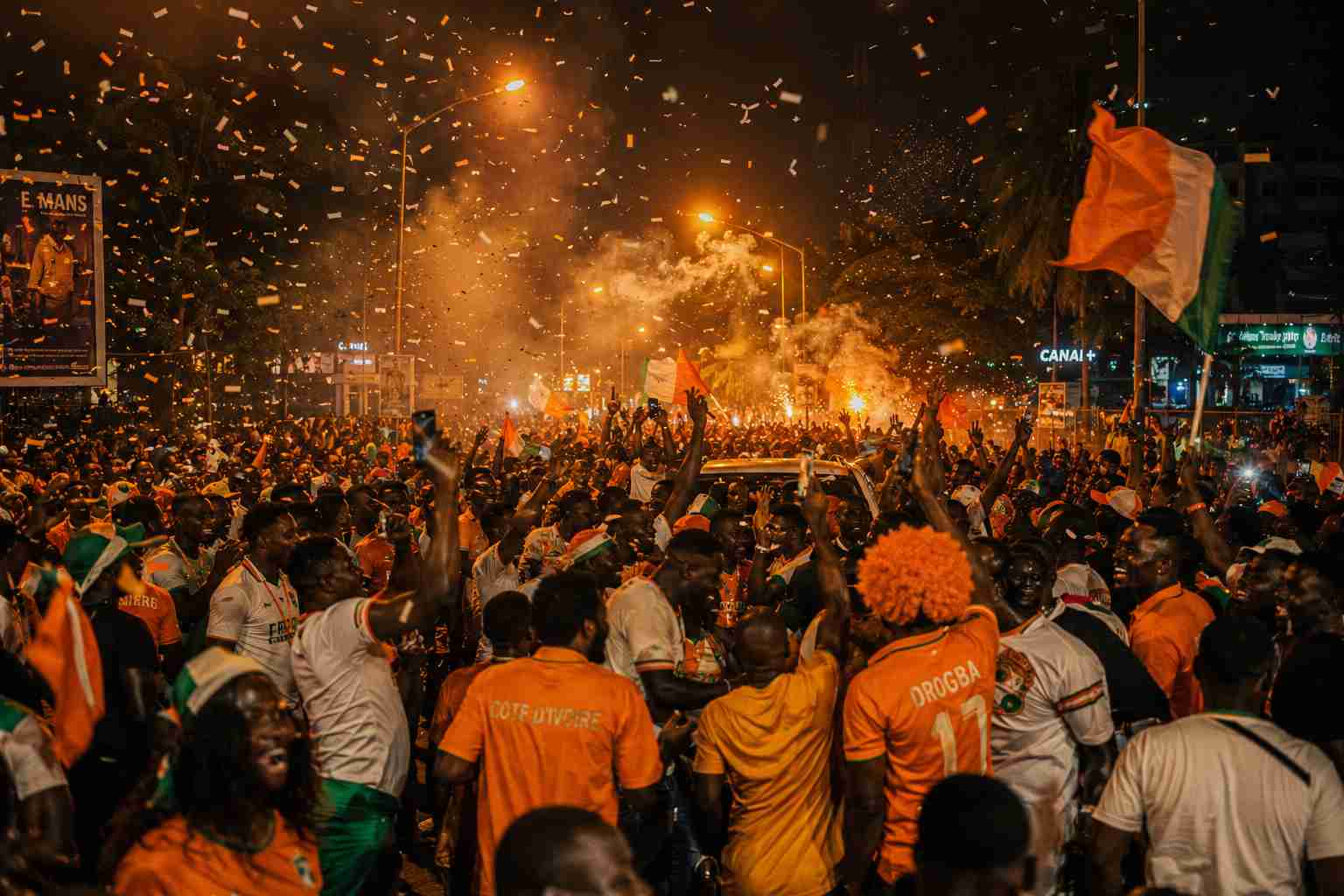 Ivorian football fans celebrating in the streets of Abidjan at night with national colours and confetti in the air